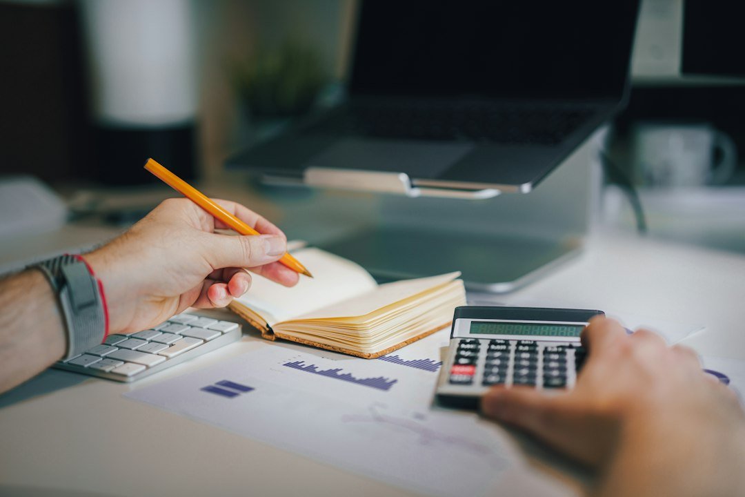 A person working with a physical calculator, notebook and printed chart at a desk